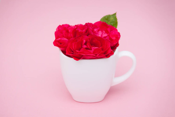 Flores rosas rojas en una taza sobre fondo rosa. Puesta plana, vista superior, fondo floral
. - Foto, Imagen