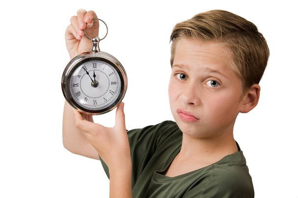 Vista lateral de cabeza y hombros de un niño caucásico de 12 años con su mano derecha sosteniendo un reloj de bolsillo de gran tamaño con un puntero de 5 minutos a 12 y mirando decepcionadamente a la cámara aislada en blanco
. - Foto, imagen
