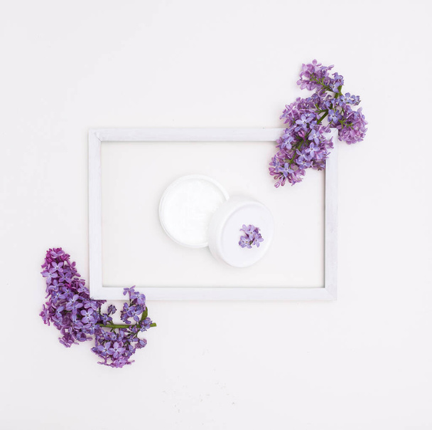 Cream in a jar in a wooden white frame on a white background and lilac flowers. Concept of skin care, Spa. - Zdjęcie, obraz