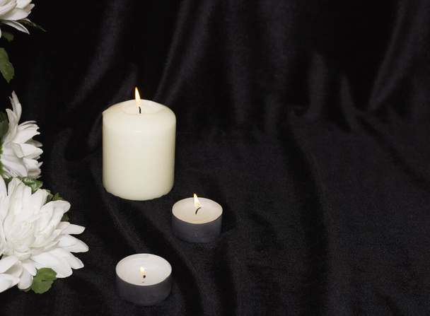 The concept of funeral service. Candles and white flowers on a black background. Free space for text. - Photo, Image