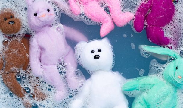 Faire tremper la poupée lapin avec un ours en peluche jouet dans un détergent à lessive avant de laver. Concept blanchisserie, Vue dessus
 - Photo, image