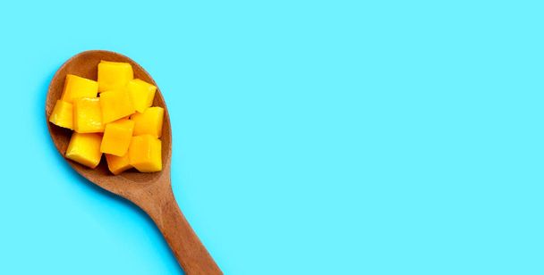 Pokrojone dojrzałe kostki mango na drewnianej łyżeczce na niebieskim tle. Przestrzeń kopiowania - Zdjęcie, obraz