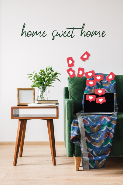 green sofa, blanket, laptop with blank screen and hearts illustration near wooden coffee table with green plant, books, photo frame and home sweet home lettering  - Foto, Bild