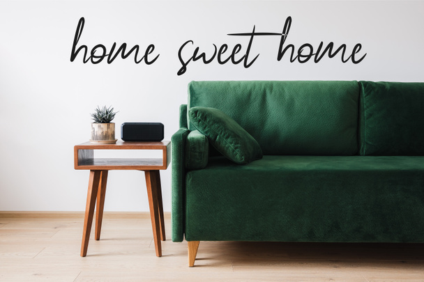 πράσινο καναπέ, μαξιλάρι, ξύλινο τραπεζάκι σαλονιού με φυτό και ξυπνητήρι κοντά στο σπίτι γλυκό σπίτι γράμματα  - Φωτογραφία, εικόνα