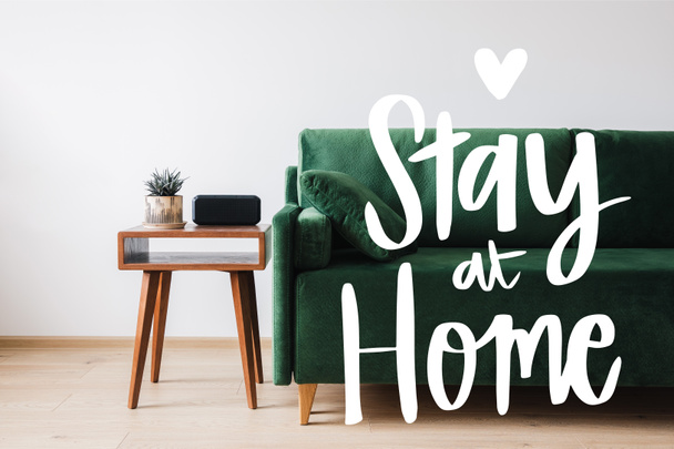 green sofa, pillow, wooden coffee table with plant and alarm clock near stay at home lettering  - Фото, изображение