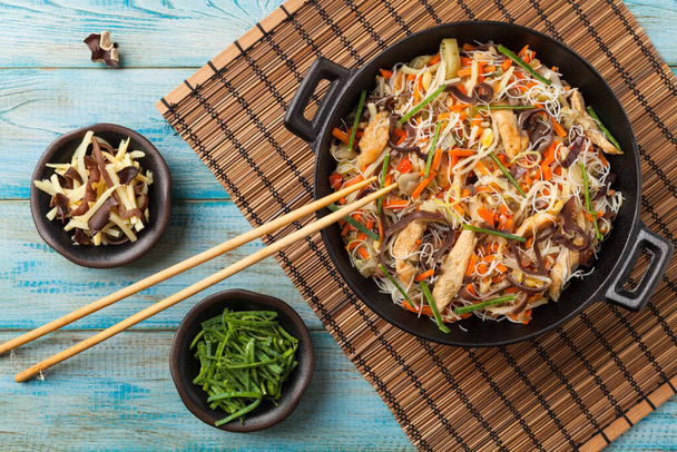 Rice noodles with chicken, mushrooms mun and vegetables, prepared in wook. Top view. - Foto, Bild