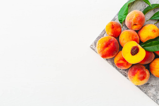 Peaches and peach in halves with leaves on white wooden background. Flat lay composition with ripe juicy peaches copy space. Harvest of peaches for food or juice. Top view fresh organic peach fruit. - 写真・画像