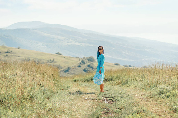 Beautiful young woman wearing in blue dress walking on rural path in summer meadow. - Фото, изображение