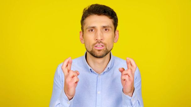 Man in light blue shirt crossed his fingers on yellow background with copyspace - Photo, Image