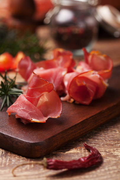 Delicious prosciutto ham on a wooden board with spices. - Фото, изображение