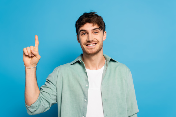 happy man looking at camera while showing idea gesture on blue - Photo, Image