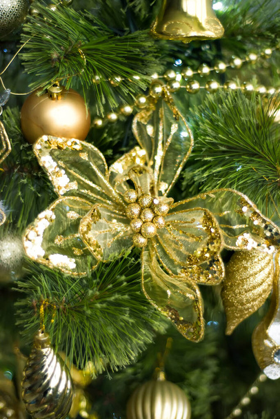 Verticale close-up foto van gouden kerstversieringen op groene kerstboom met grote gouden kunstbloem aan de voorkant. Gelukkig Nieuwjaar en vrolijk kerstfeest. Selectieve focus. Wintervakantie. - Foto, afbeelding
