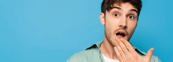 panoramic shot of shocked young man looking at camera isolated on blue - Photo, image