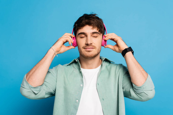 boldog fiatalember megérinti vezeték nélküli fejhallgató közben zenét hallgatni a kék - Fotó, kép