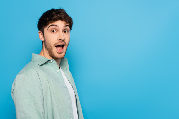 shocked young man with open mouth looking at camera isolated on blue - Foto, Imagem
