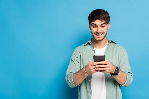 cheerful young man chatting on smartphone on blue - Photo, Image