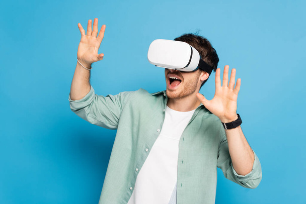 excited young man gesturing while using vr headset on blue - Fotoğraf, Görsel