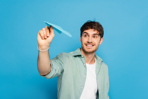 allegro giovane uomo lanciando aereo di carta su blu - Foto, immagini