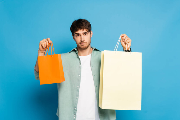 thoughtful young man showing shopping bags on blue - Photo, Image