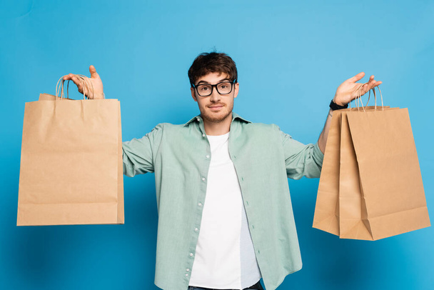 handsome young man holding shopping bags on blue - Valokuva, kuva