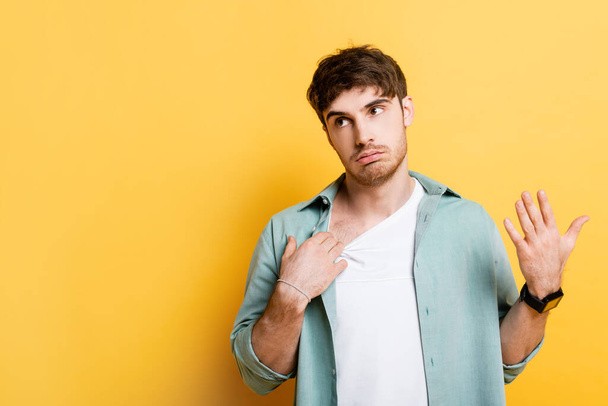 displeased young man touching shirt and waving hand while suffering from heat on yellow - 写真・画像
