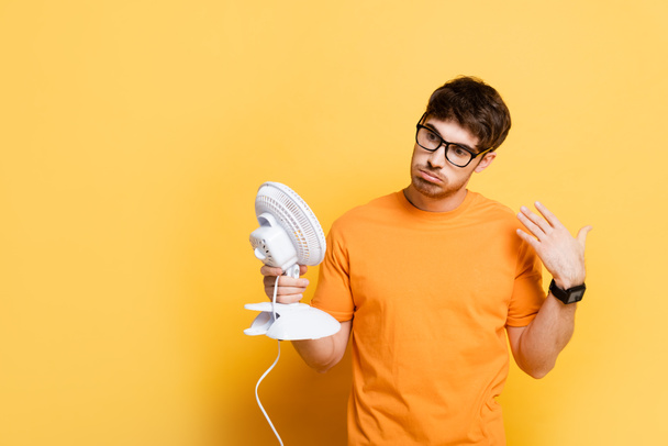 hombre disgustado sosteniendo ventilador eléctrico y agitando la mano en amarillo
 - Foto, imagen