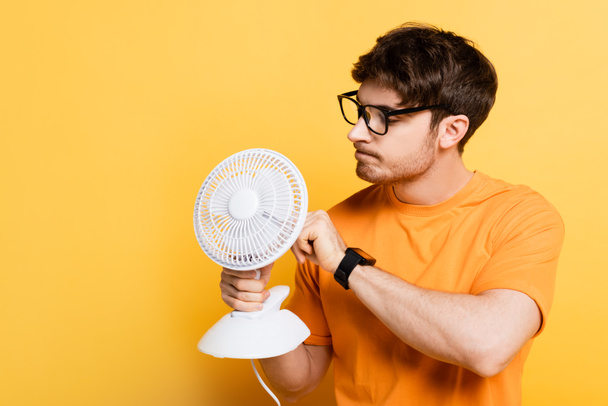 thoughtful young man fixing electric fan on yellow - Фото, изображение