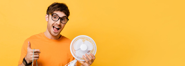 excited man in eyeglasses holding shopping bag with new electric fan on yellow, website header - Photo, image