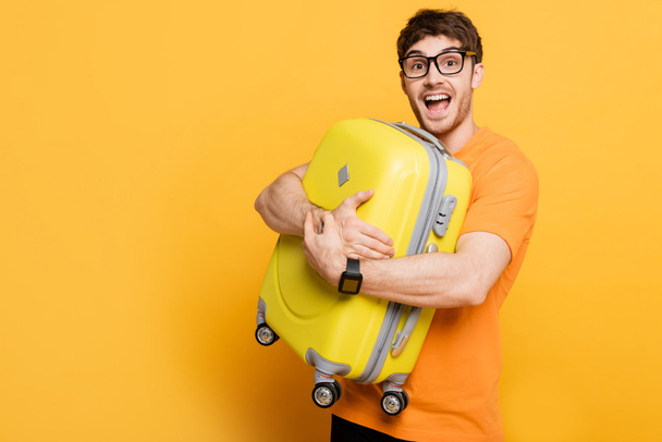 excitado turista masculino que sostiene la maleta para las vacaciones de verano en amarillo
  - Foto, Imagen