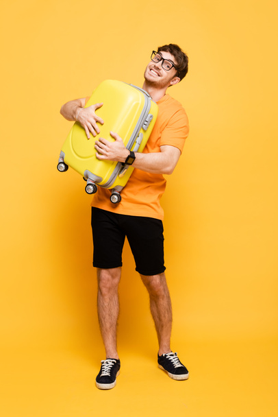 smiling male tourist holding suitcase for summer vacation on yellow  - Foto, afbeelding