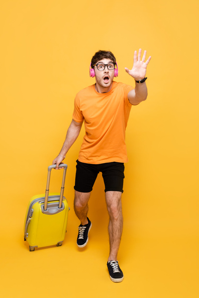 late schreeuwende man in koptelefoon loopt met reistas op geel - Foto, afbeelding
