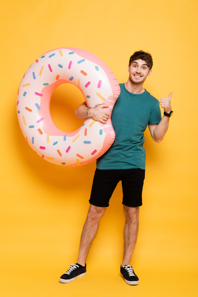 happy man showing thumb up while standing with inflatable donut on yellow  - Photo, Image