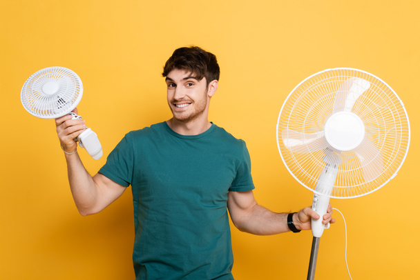 šťastný muž stojící se dvěma elektrickými ventilátory na žluté    - Fotografie, Obrázek