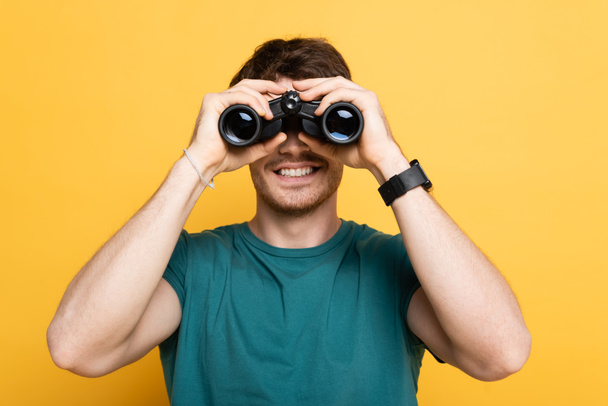 cheerful man looking through binoculars on yellow - Photo, Image