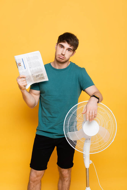surullinen mies kärsii lämpöä sähköinen tuuletin ja sanomalehti käsi tuuletin keltainen     - Valokuva, kuva