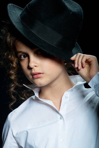adorable preteen girl posing with hat on black background - Фото, изображение