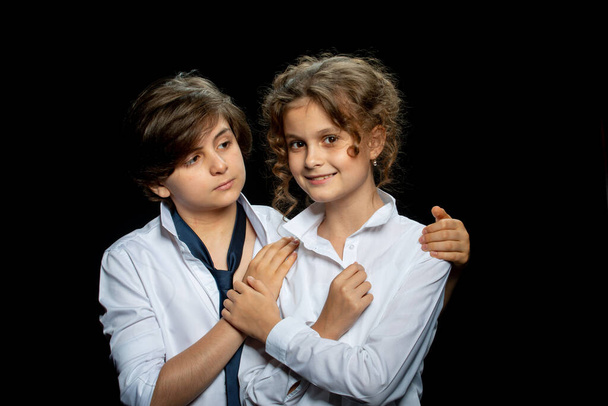 preteen boy and girl in white shirts posing in studio on dark background and hugging - Foto, Imagem