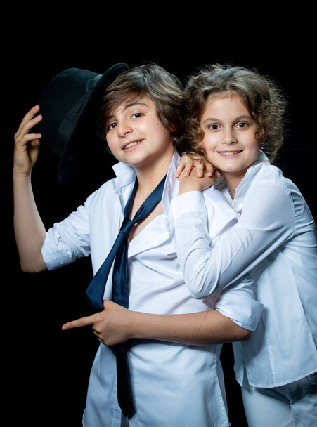 preteen boy and girl in white shirts posing in studio on dark background and hugging - 写真・画像