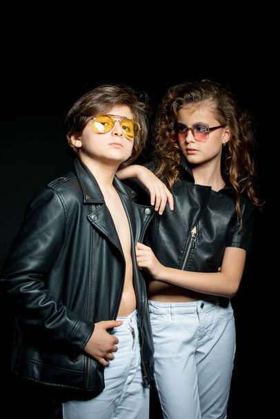 preteen boy and girl in leather clothes posing in studio on dark background - 写真・画像
