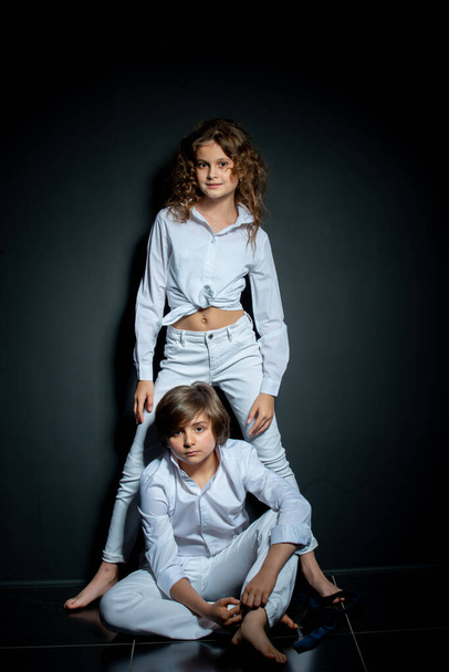preteen boy and girl in white shirts posing in studio on dark background - Valokuva, kuva