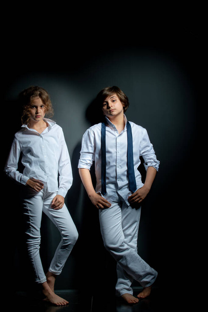 preteen boy and girl in white shirts posing in studio on dark background - Photo, Image