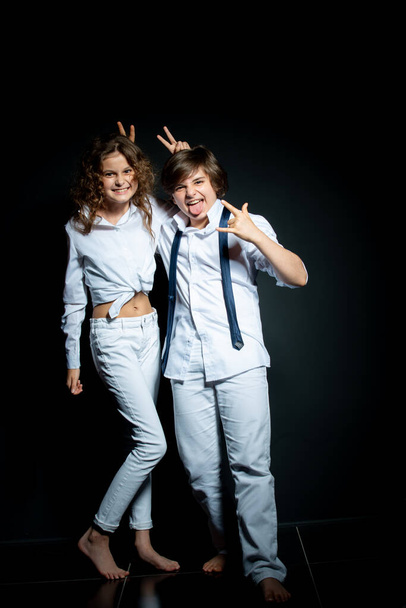 preteen boy and girl in white shirts posing and having fun in studio on dark background - Photo, image
