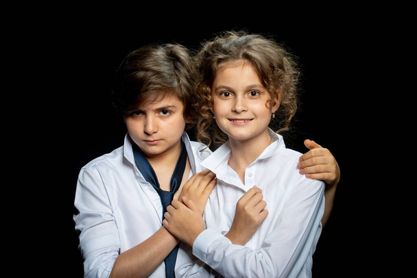 preteen boy and girl in white shirts posing in studio on dark background and hugging - Foto, Imagen