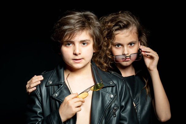 preteen boy and girl in leather clothes posing in studio on dark background - Photo, Image