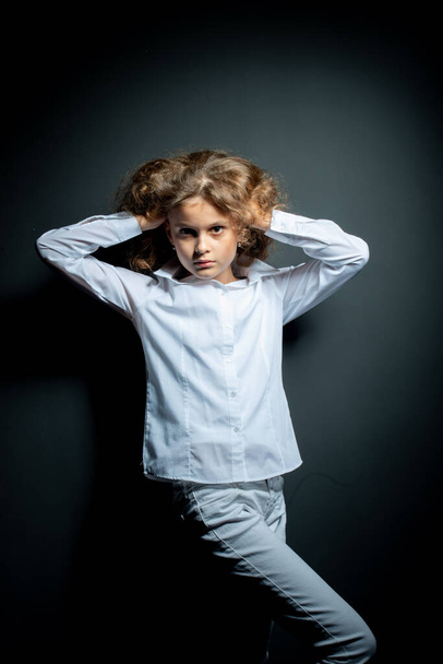 adorable preteen girl in white shirt posing on dark background and looking at camera - Photo, Image