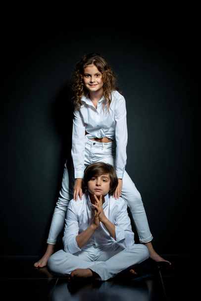 preteen boy and girl in white shirts posing in studio on dark background - Foto, afbeelding