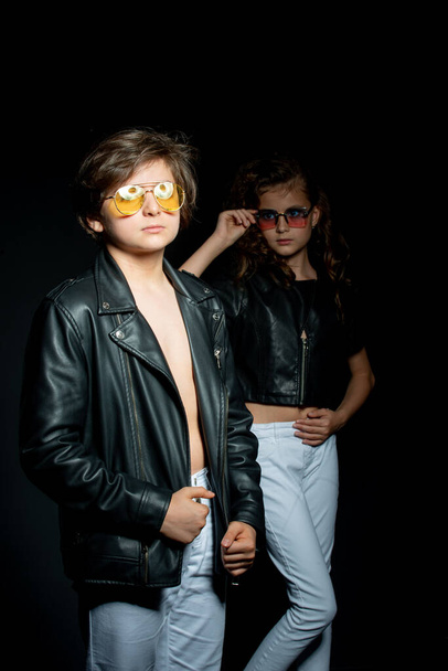 preteen boy and girl in leather clothes posing in studio on dark background - Photo, image