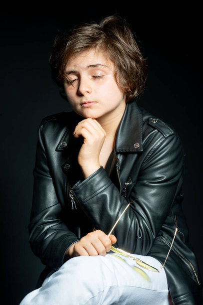 preteen boy in black leather jacket posing on black background - Фото, изображение