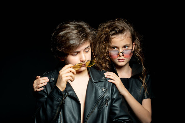 preteen boy and girl in leather clothes posing in studio on dark background - Zdjęcie, obraz