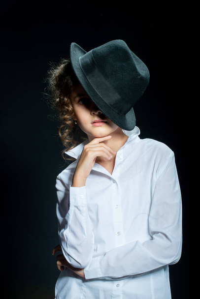 adorable preteen girl posing with hat on black background - 写真・画像